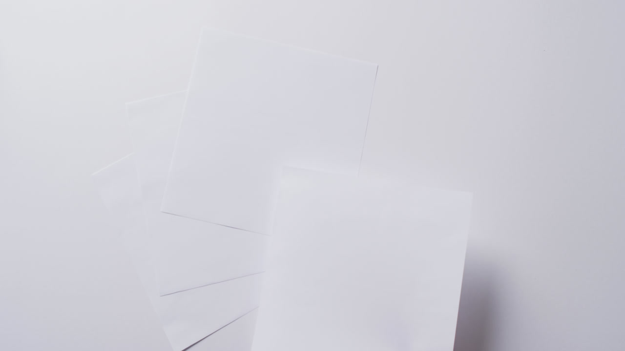 Hand holding piece of paper over pieces of paper with copy space on white background in slow motion