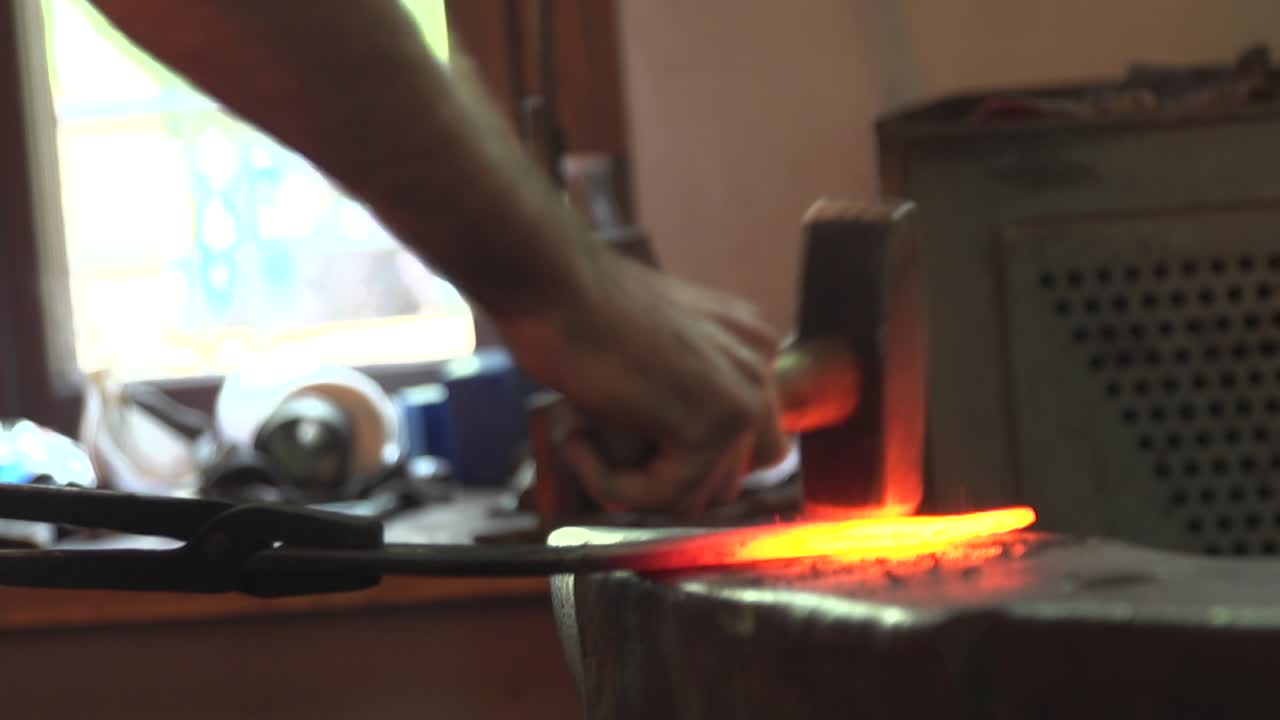 forjar una pieza de metal caliente con un martillo en un lugar de trabajo de herrero