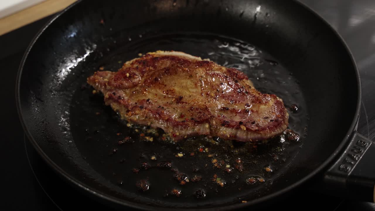Bistecca di manzo condita scottata, girata in padella calda con olio, che forma una superficie dorata e arrostita sulla parte superiore.