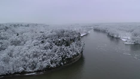 Aerial-view-of-vast-snow-covered-forest-on-a-hill-next-to-lake,-Winter-season-concept