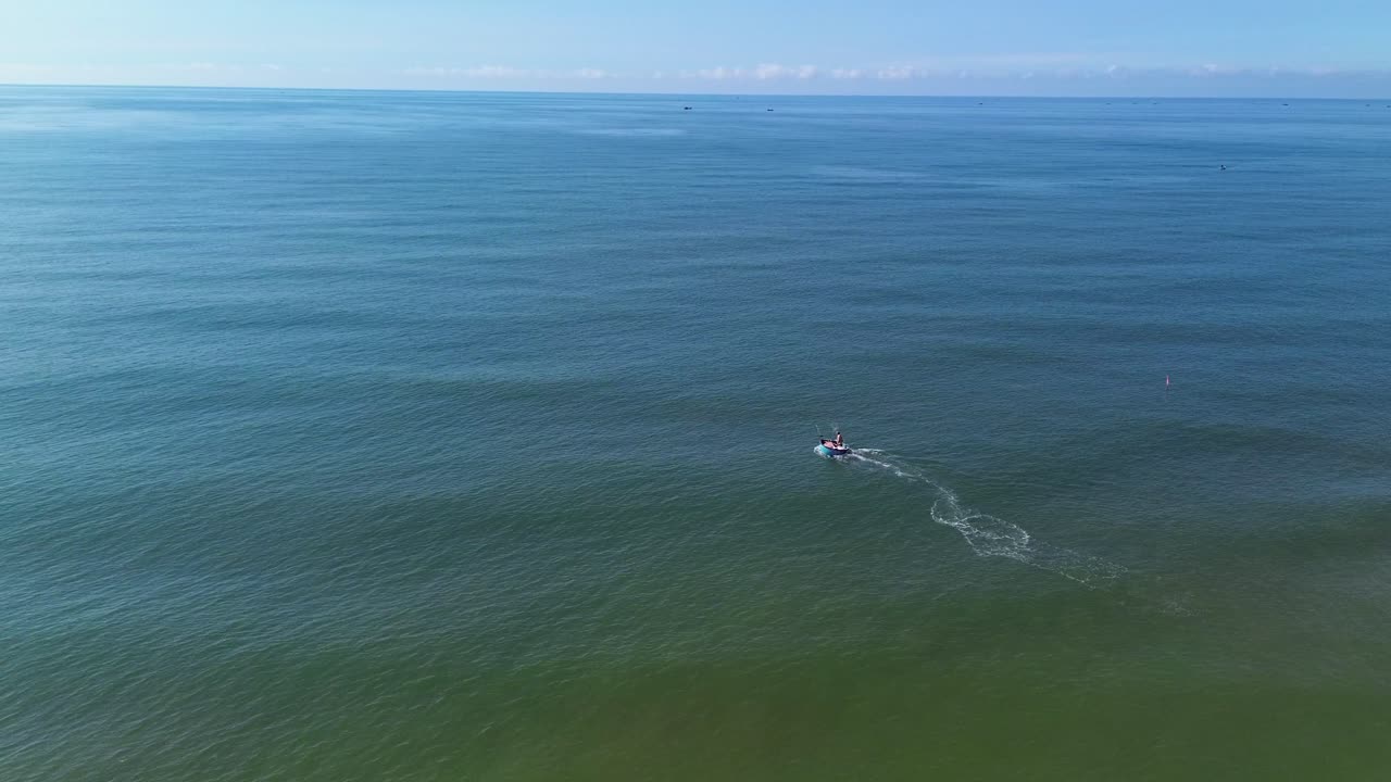 Drone captures a small boat cruising from right to left along the calm sea near Mui Ne, Vietnam, with a glowing sunset horizon in the background and peaceful ocean vibes.