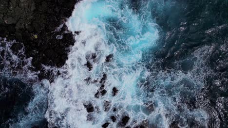 Birds-Eye-view-of-small-waves-breaking-over-black-volcanic-rock-in-Bali