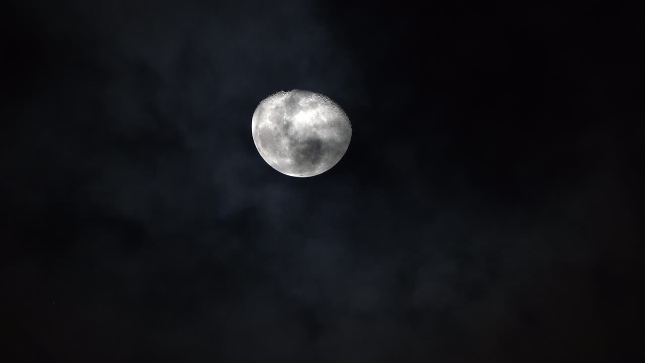 brillantes cráteres y crestas blancas de la luna se levantan en el cielo a medida que las nubes pasan por debajo por la noche