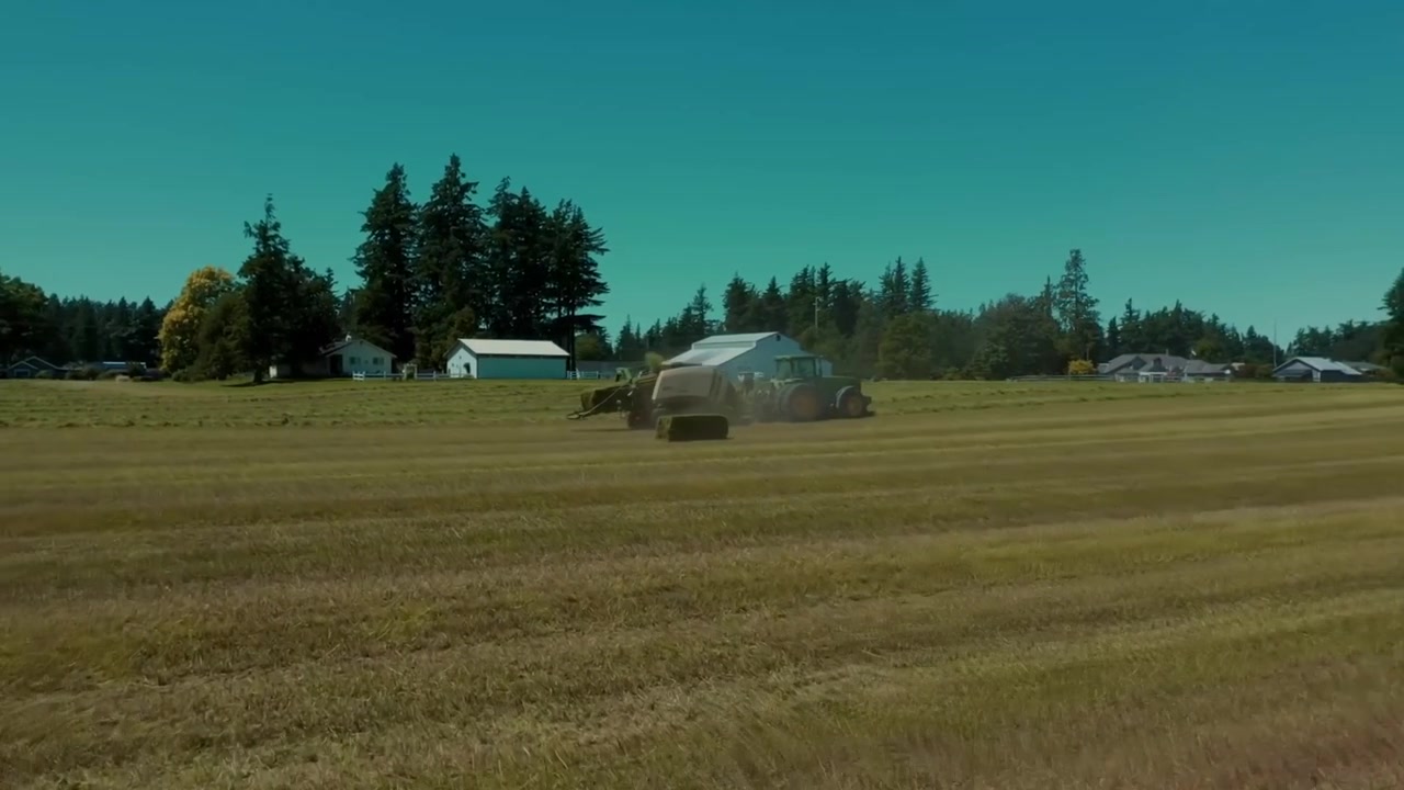 Fluida ripresa cinematografica con drone in tracking che vola verso un trattore moderno che ara un campo agricolo nella campagna britannica. Macchinari per l'agricoltura di precisione che coltivano terreno fertile, mostrando l'efficienza.