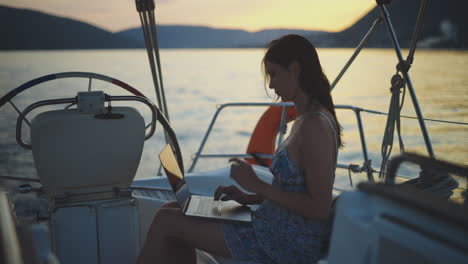 woman working on laptop on a yacht at sunset