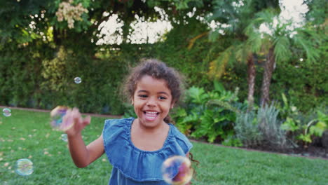 Young-Hispanic-Girl-Chasing-And-Catching-Bubbles-In-Garden