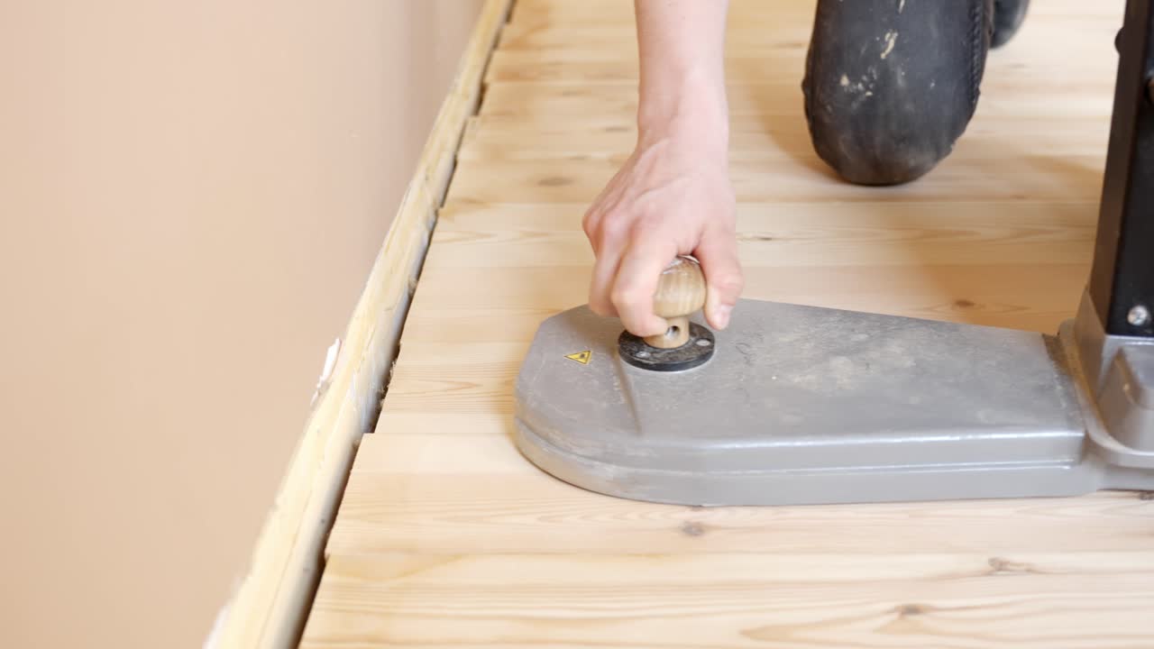 Manual precise movements of sander across wooden floor near wall using, detailed close up
