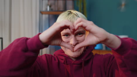 happy blonde young woman makes symbol of love showing heart sign to camera express romantic feelings