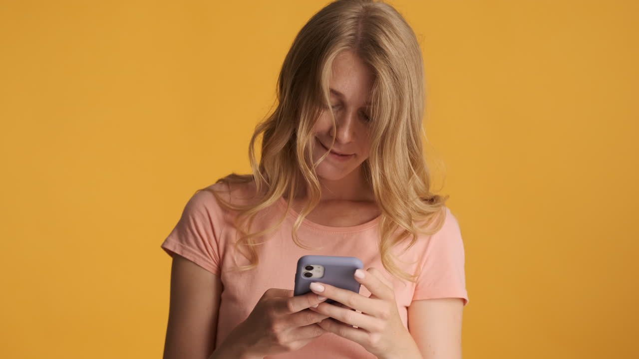 una mujer caucásica usando un teléfono inteligente y confundiéndose con la cámara.