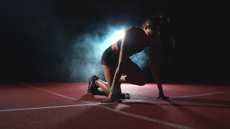 Young-woman-athlete-in-black-shorts-and-a-t-shirt-is-preparing-to-start-in-the-race-for-100-meters-on-the-treadmill-near-the-start-line