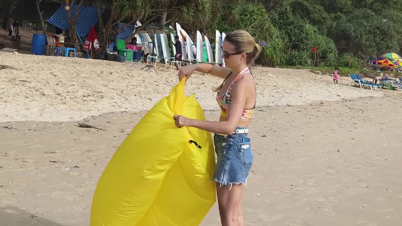 женщина упаковывает надувной лежачок на пляже