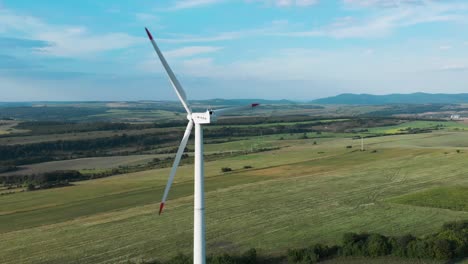 aerial panoramic shot around single wind turbine generator in grass field