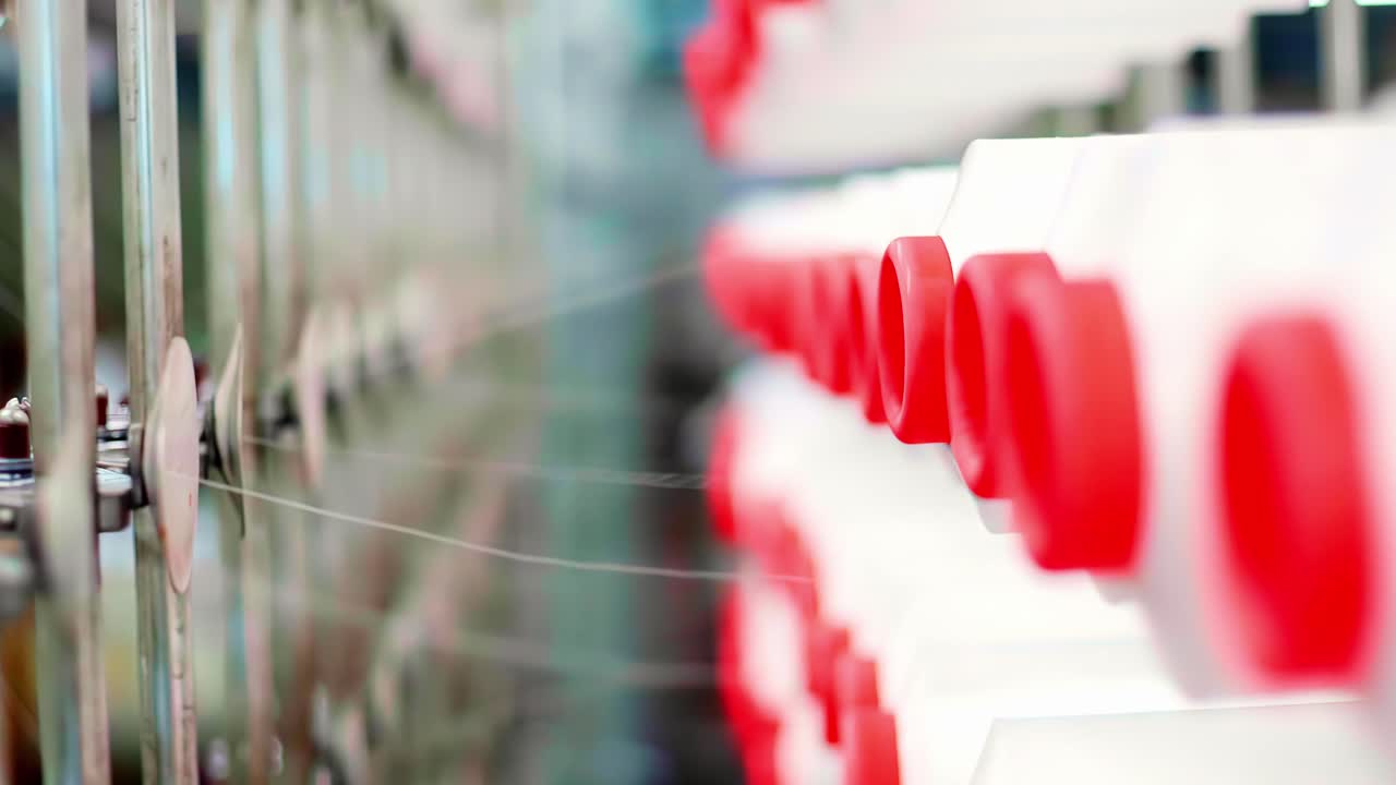 A macro close-up shot with a shallow depth of field shows fine white threads being processed at high speed by an automated spinning loom in a modern textile factory