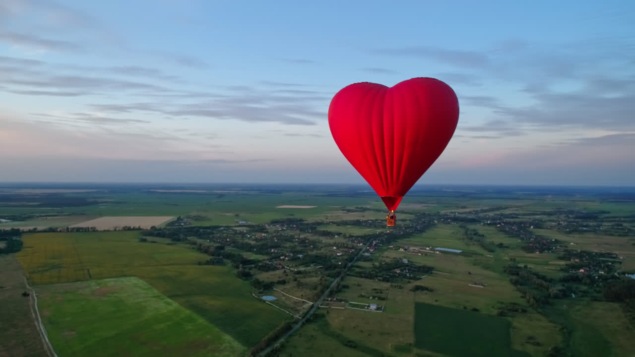 Red airship in the shape of a heart. Hot air balloon in the sky over a field in the countryside flying in the beautiful evening sky.