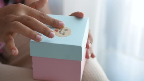 hands holding a light blue and pink gift box with a thank you note