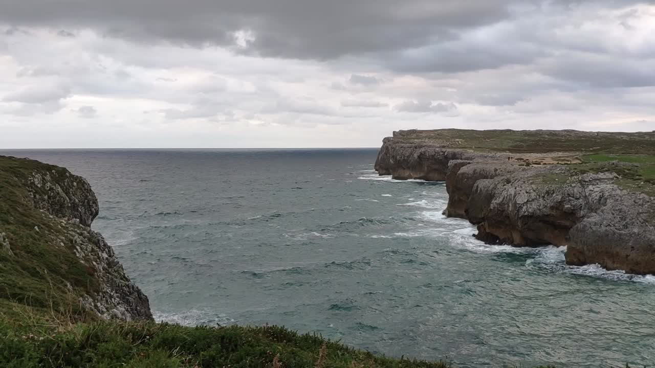 Rocky cliffs meet the ocean under a cloudy sky at Guadamia, Asturias coast