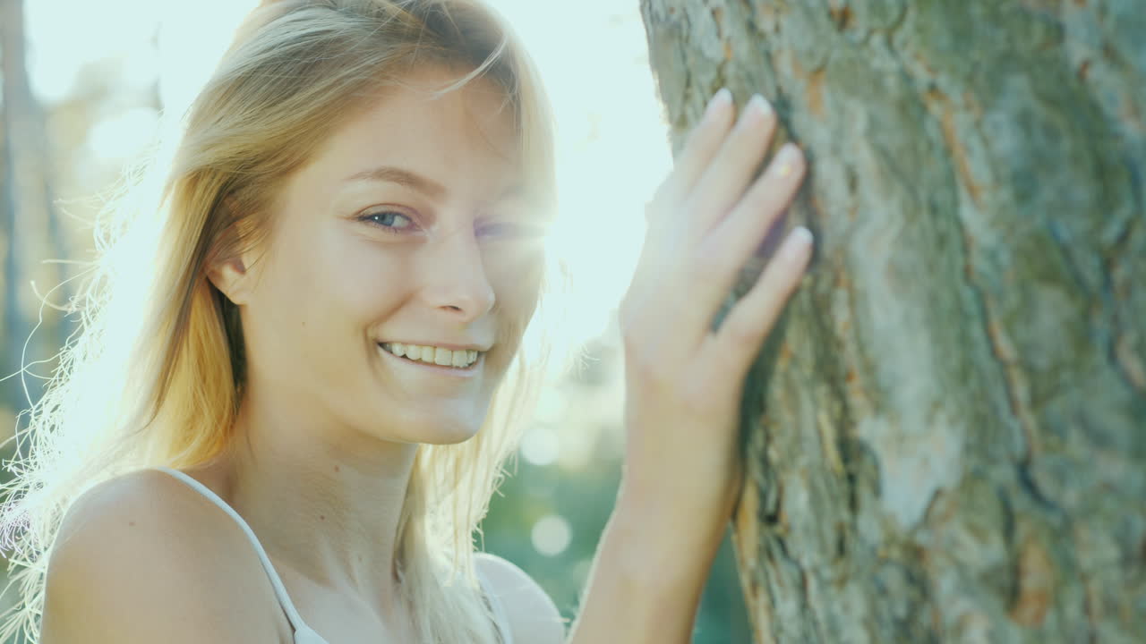 카메라 co를 보고 웃 고 태양에서 나무에 의해 서 있는 아름 다운 젊은 여자의 초상화