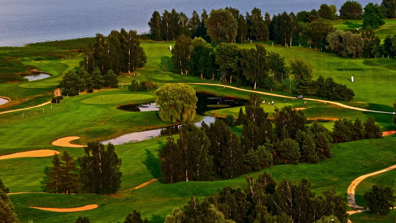 Üppig grüner Golfplatz an einem ruhigen See bei Sonnenuntergang.