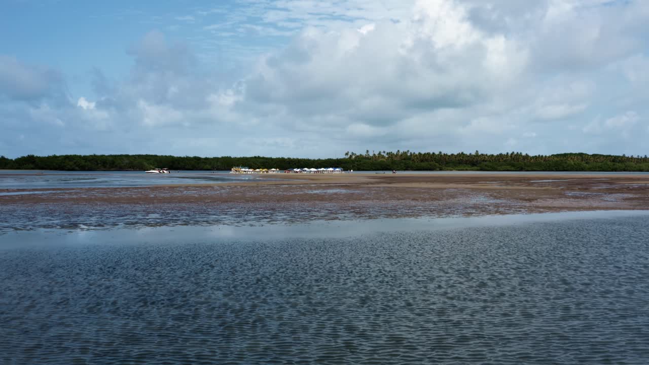 Dolly in aerial drone shot approaching a natural sand bar bank on the tropical Guara&iacute;ras Lagoon with tour boats, umbrellas and food carts for tourists in Tibau do Sul, Brazil in Rio Grande do Norte