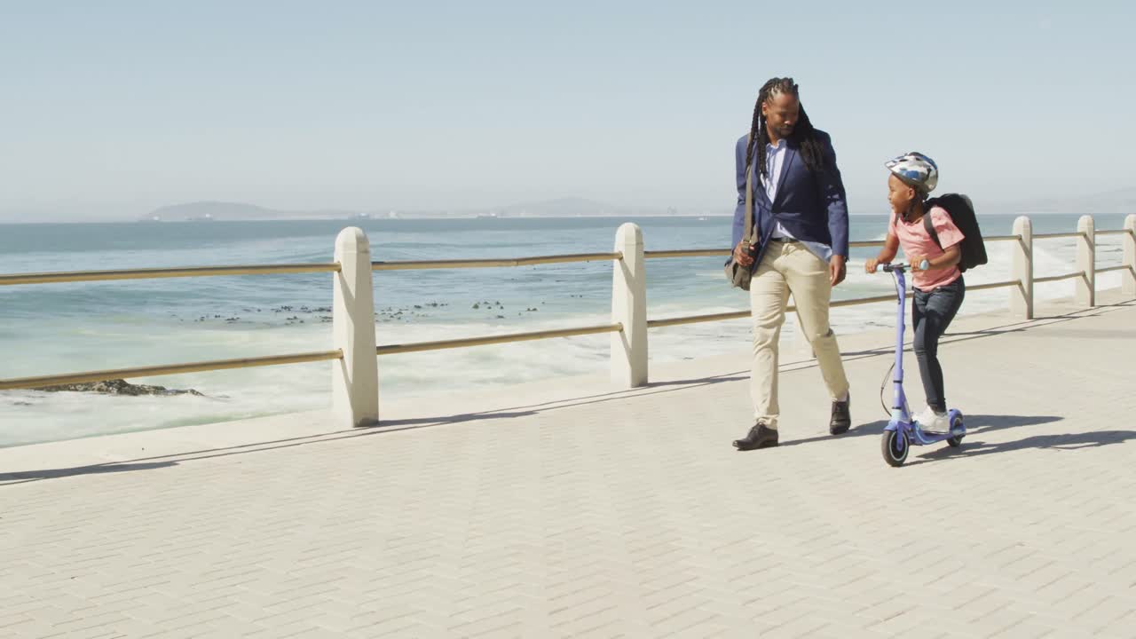 video de un feliz padre e hijo afroamericanos en scooter pasando tiempo en el mar