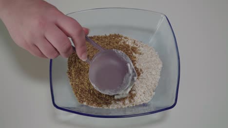 adding flour to flax and quick oats in glass mixing bowl, overhead closeup