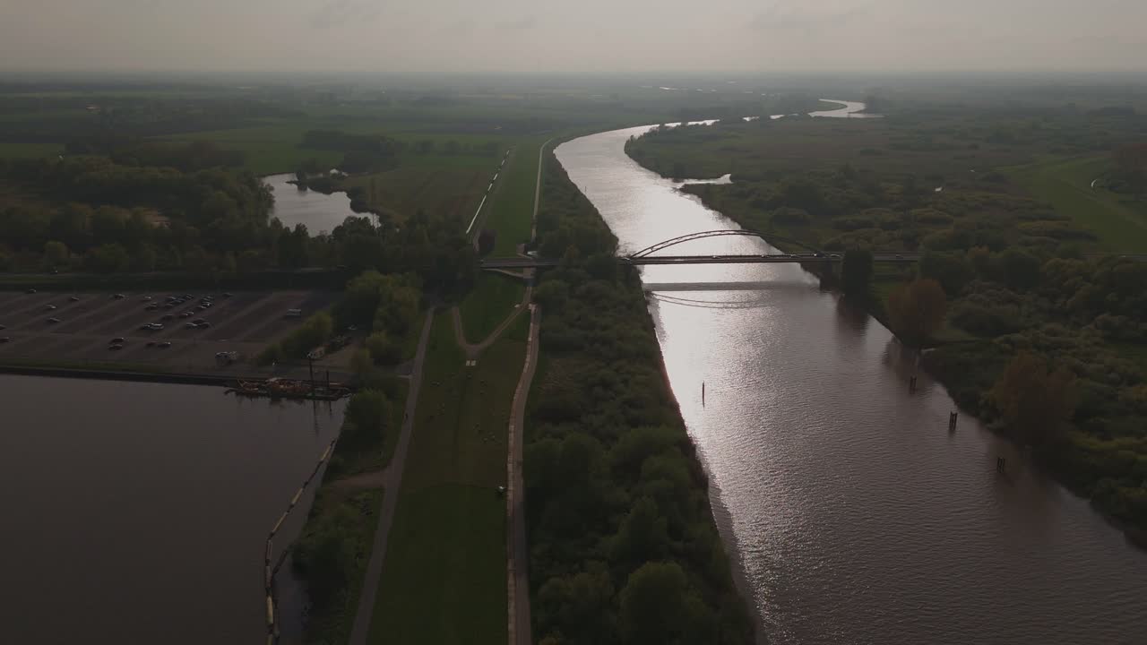 Aerial shot of a bridge crossing the Ems River near the Meyer Werft shipyard at sunset. Scenic river bend, dikes, and green landscape in soft evening light. Shot in 4K.