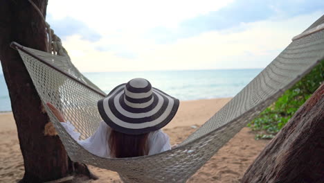 woman in hammock, wearing sunhat looking towards ocean