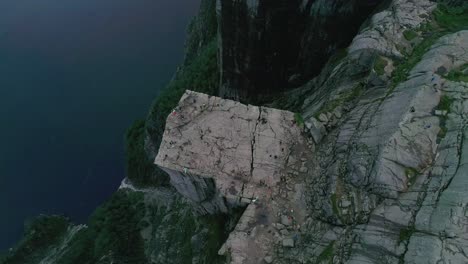 toma aérea en cámara lenta de preikestolen, noruega, dando vueltas alrededor de los turistas caminando y fotografiando el paisaje
