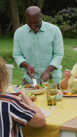video vertical de una familia feliz y diversa cenando en el jardín