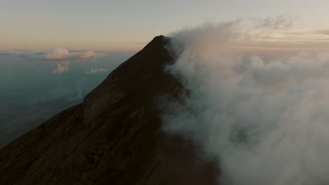 Tilt-up-aerial-of-Fuego-volcano-covered-by-clouds-during-sunset-in-Guatemala