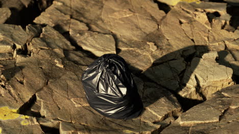 black trash bag lay on a rocky beach