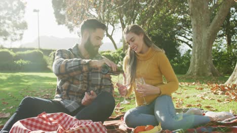 video de una feliz pareja caucásica vestida cálidamente bebiendo vino en el jardín