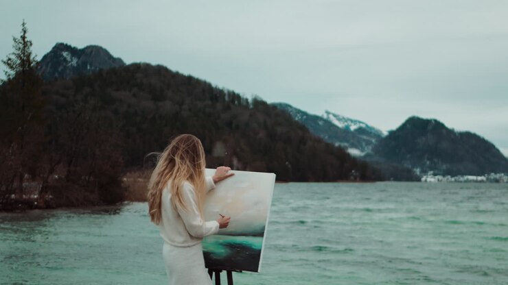 Artist painting a lake scene by the mountains