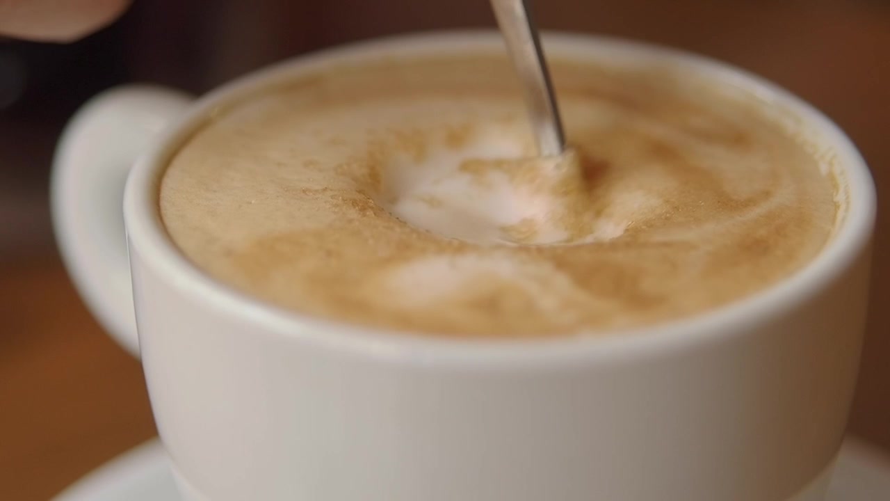 Primo piano di un cucchiaio che mescola lo zucchero in un caffè schiumoso