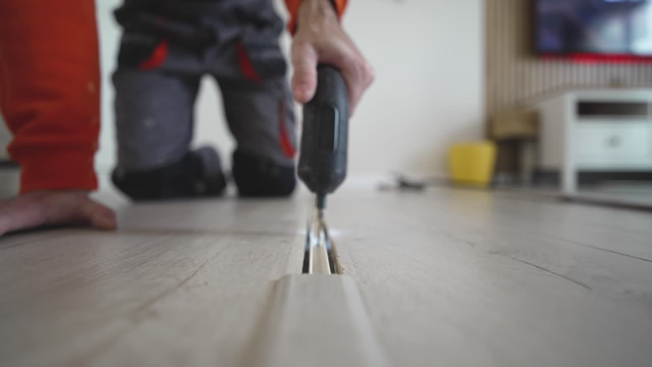Man kneels on the floor while fixing a floor transition strip using a screwdriver, highlighting home renovation, flooring installation, and DIY lifestyle work