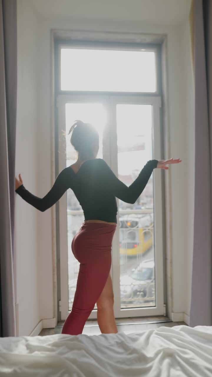 mujer estirándose y bailando en el dormitorio junto a la ventana