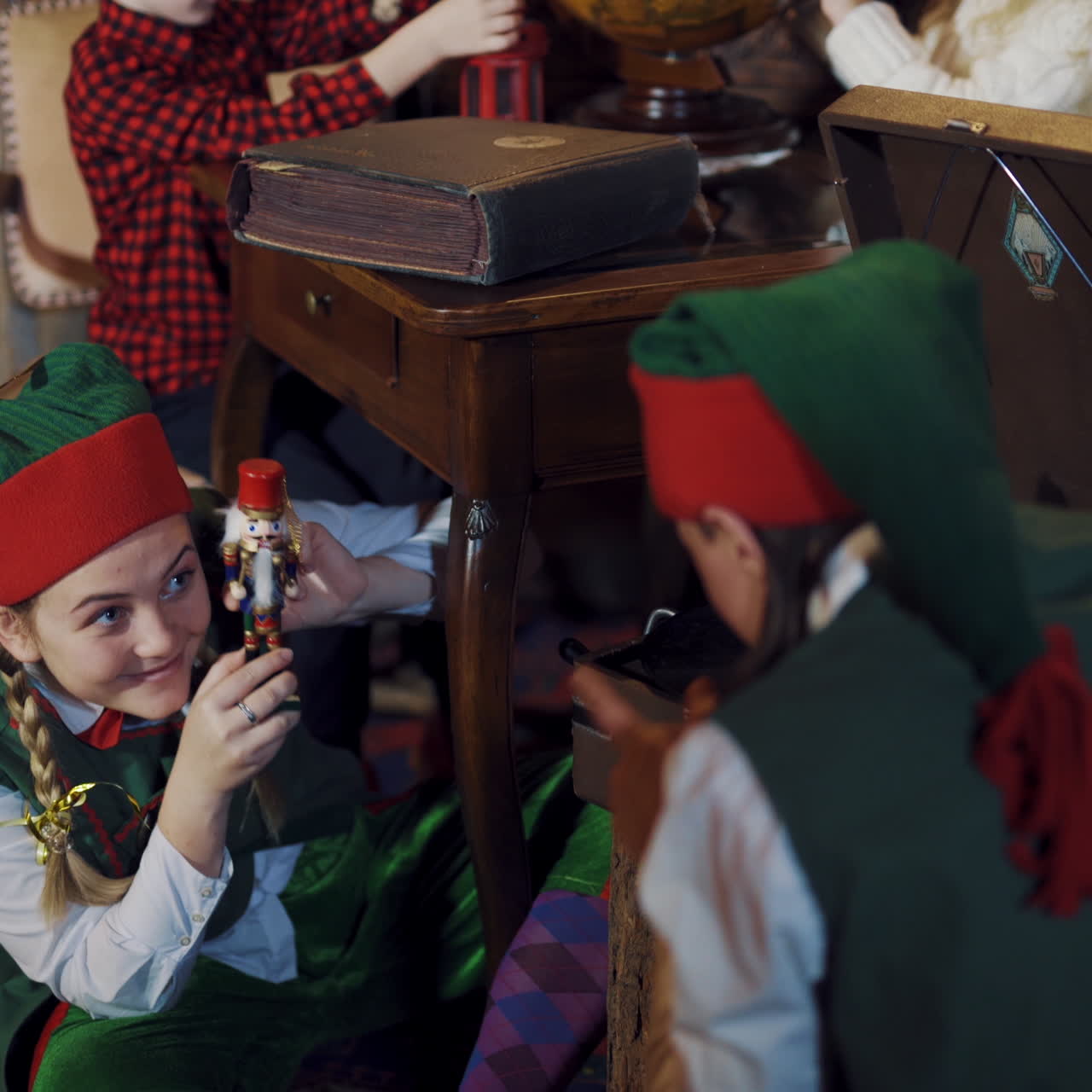 Fairy characters in green costumes play with a toy at Christmas. Happy female elf holding a toy soldier and shows it to another elf in the room.
