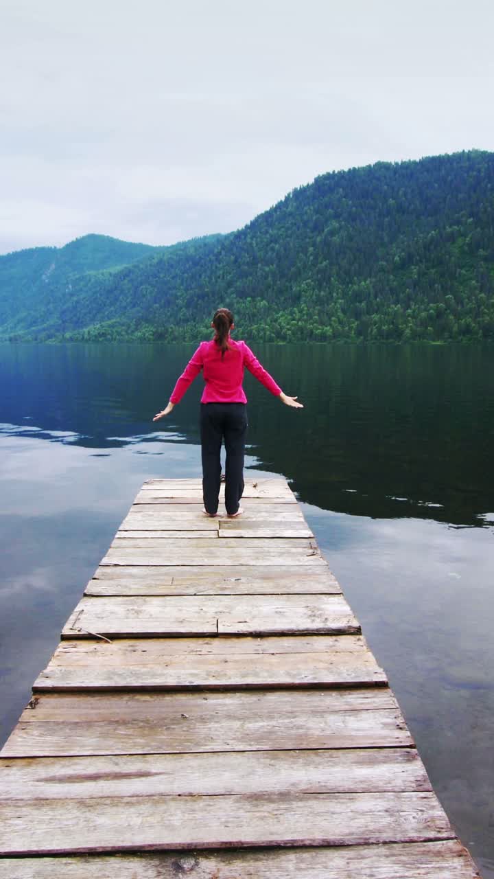 Woman practicing yoga on a wooden dock overlooking a serene lake