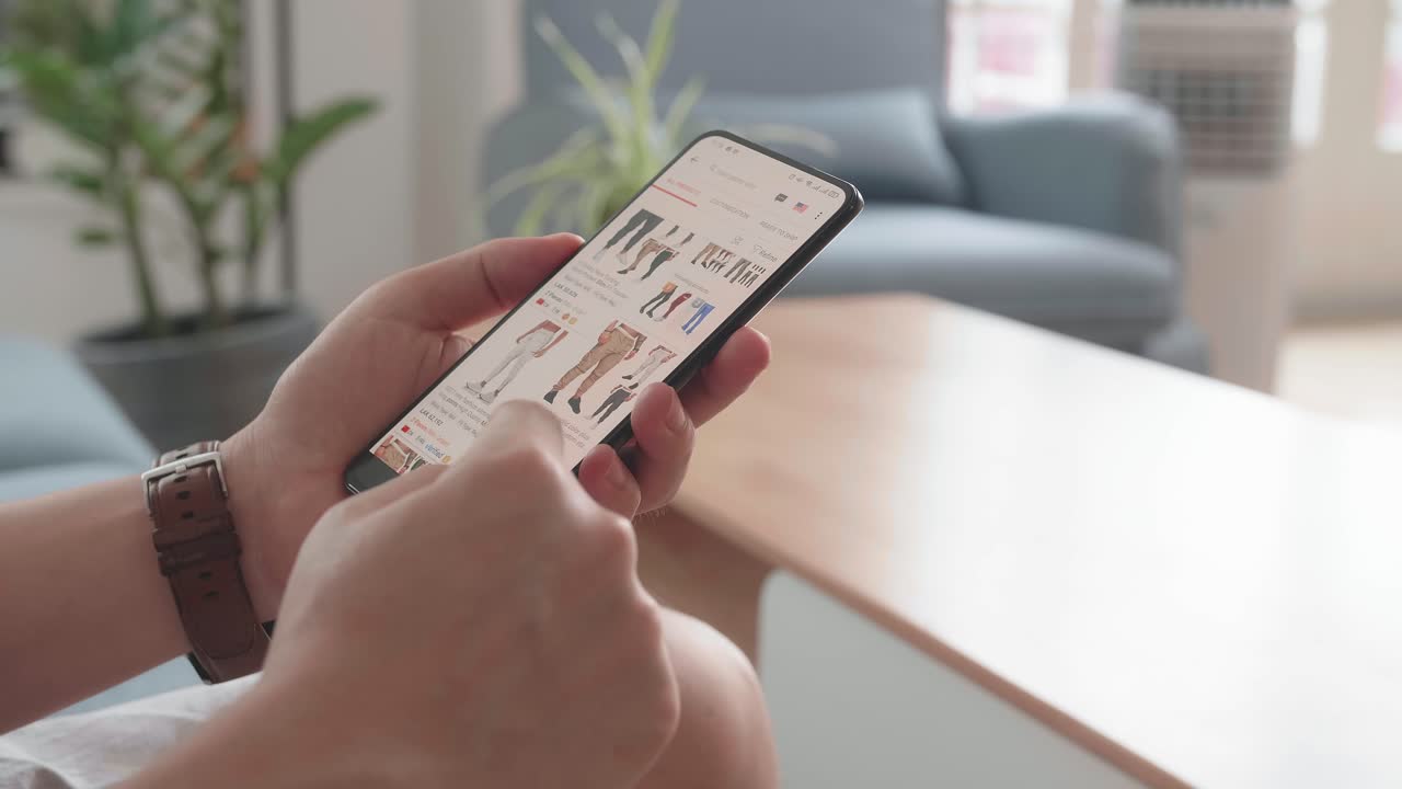 Close Up Of Man Hand Holding Smartphone And Doing Online Shopping At Home, Male Looks At Goods In Online Store Clothing