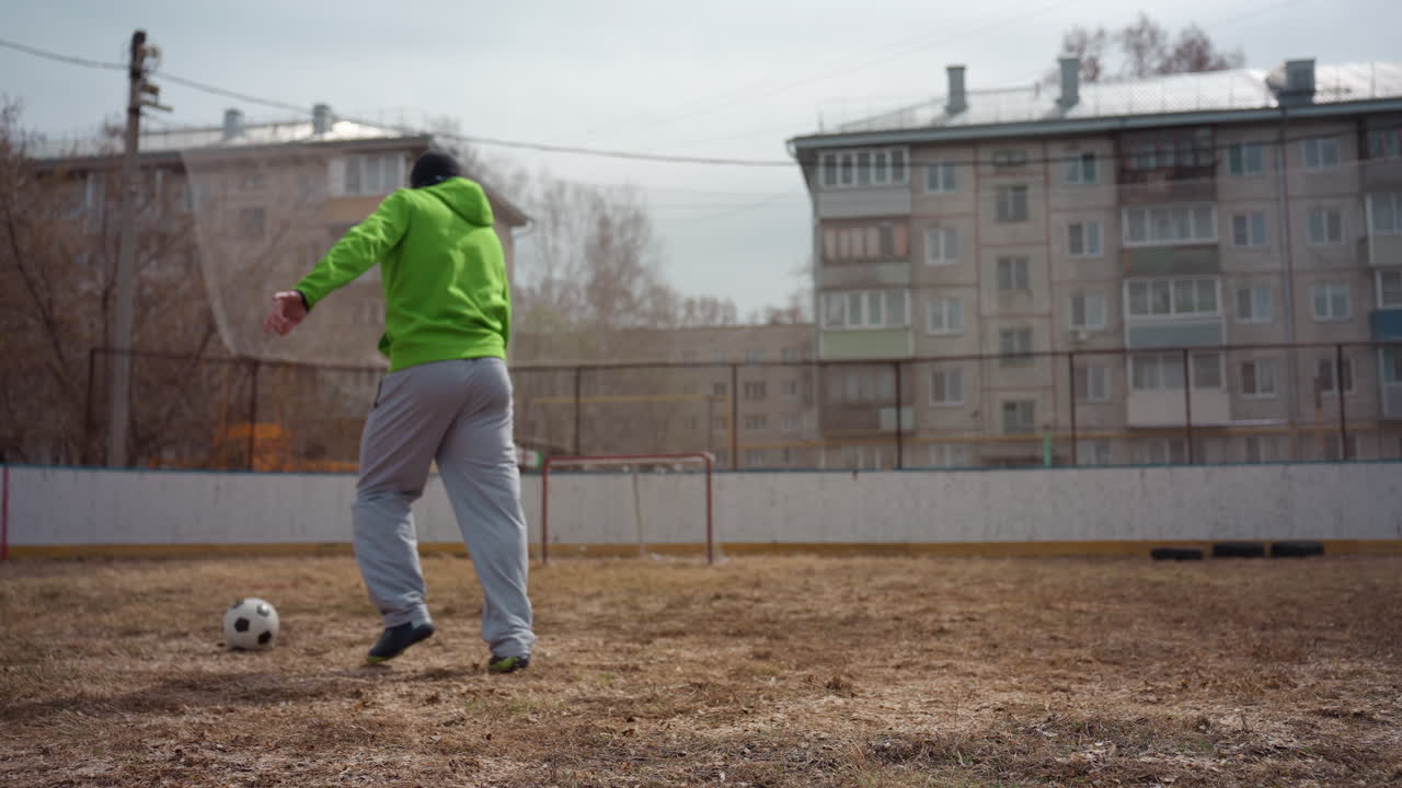 초록색 후드티를 입은 백인 남성의 코트야드 프리스타일 세션, 클로즈업 풋워크와 저글링 샷, 흙밭과 아파트 단지, 캐주얼 스니커즈와 편안한 리듬, 장난기 넘치는 도시 기술 연습