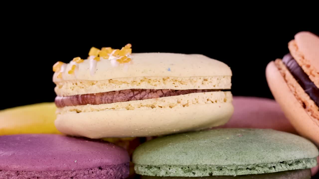 A hand reaches into the frame to select a yellow macaron from a colorful pile
