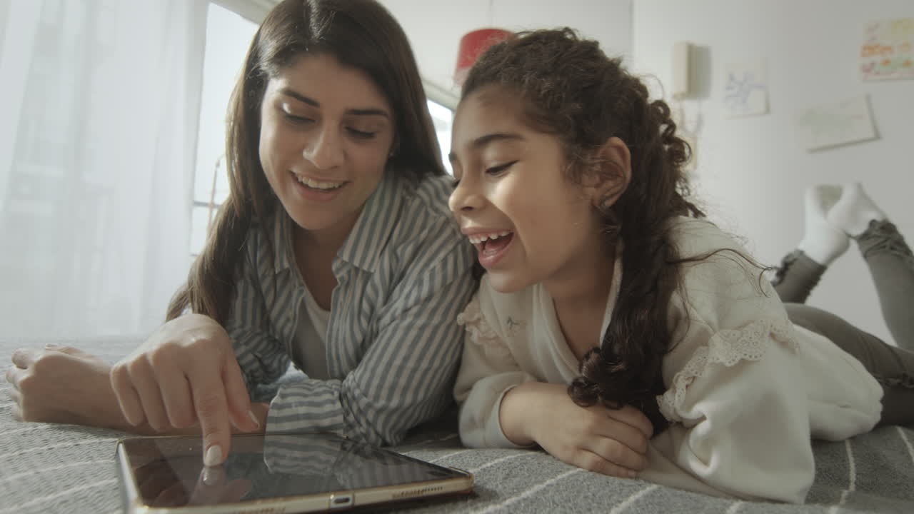 Little Girl and Mother Playing on Tablet on Bed
