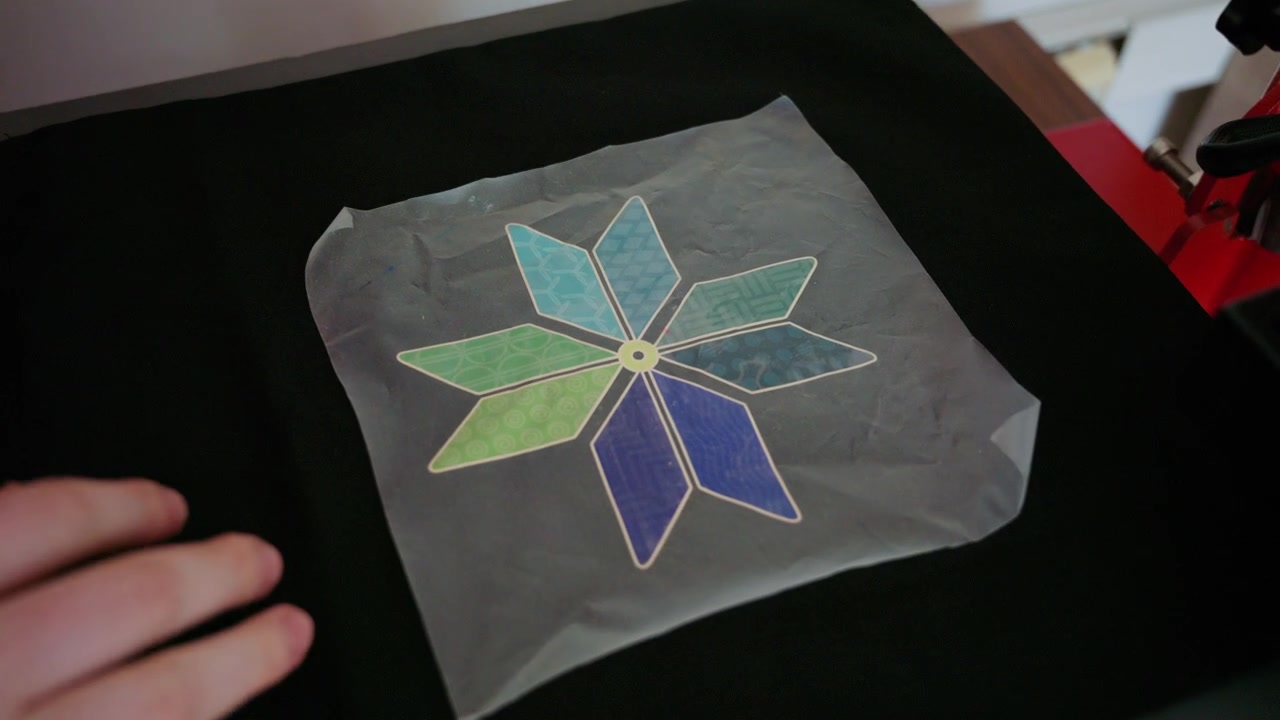 Hands placing a colorful floral heat transfer design onto black fabric and heat pressing