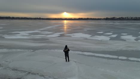 person walking on a frozen lake cinematic view with a cool sunset on the background