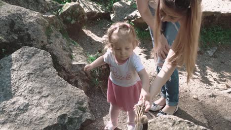 young beautiful mother with her daughter feeding a chipmunk in the woods among stones 3