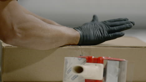 person wearing gloves seals cardboard box with tape