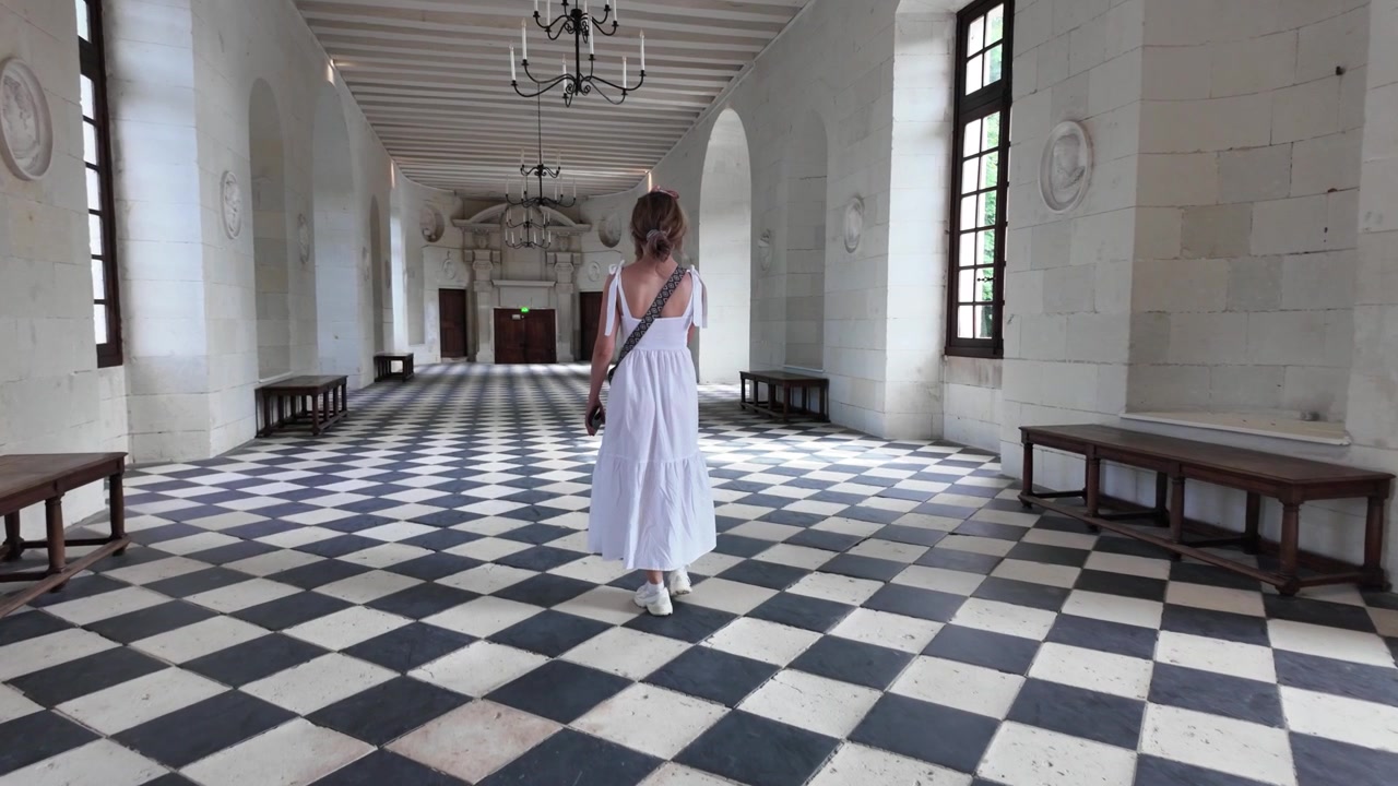 Zpomalené video cestovatelky procházející ikonickou Velkou galerií uvnitř zámku Chenonceau, s proslulou černobílou šachovnicovou podlahou