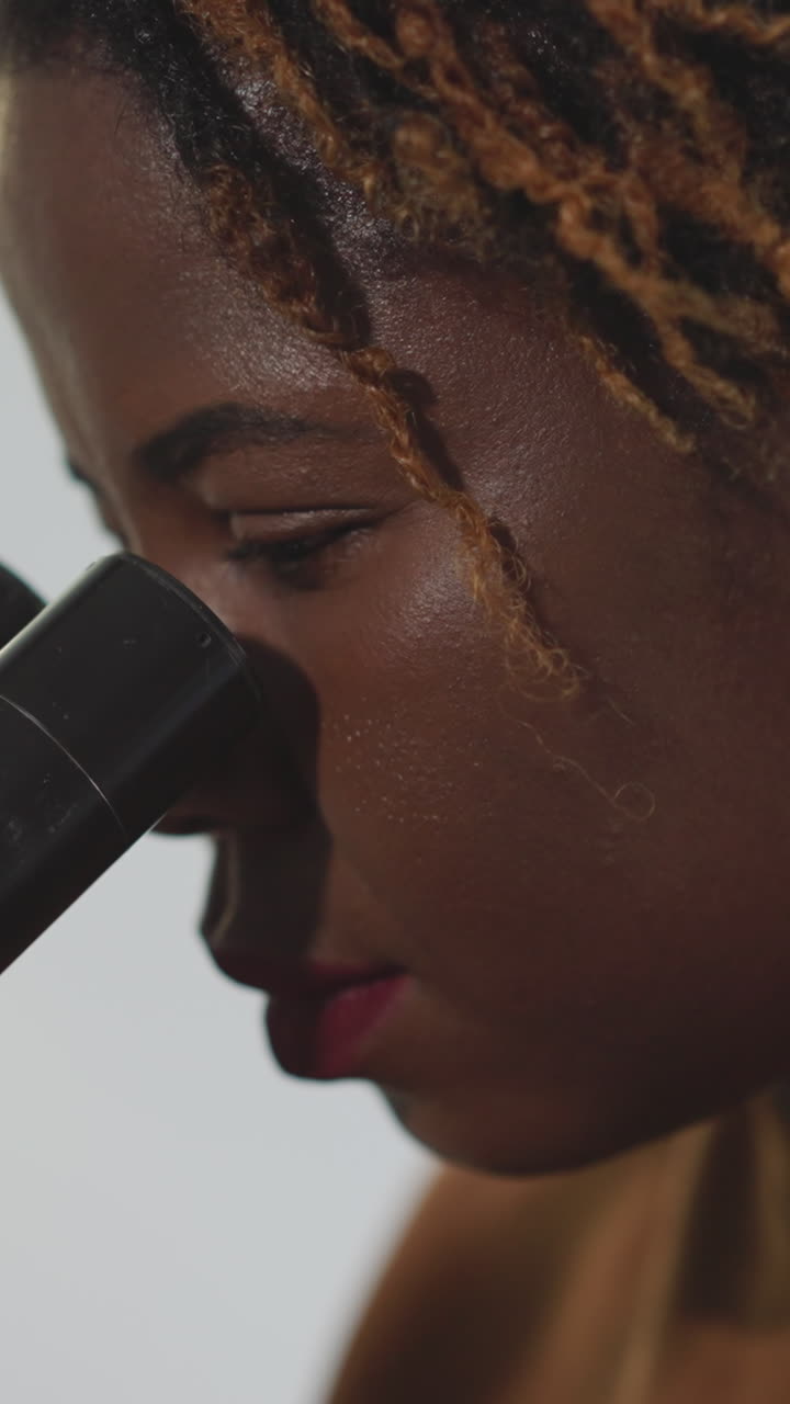 Focused African American woman examines bacteria through microscope. Female student uses professional equipment for medical research closeup