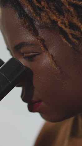 focused african american woman examines bacteria through microscope. female student uses professional equipment for medical research closeup