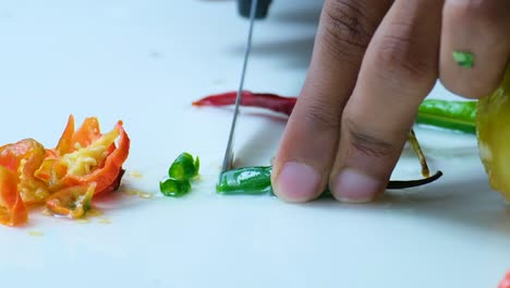 an apprentice chef slicing a green chili on white cutting board with other ingredients for a salad